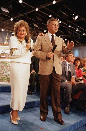 A televangelist couple on a television studio stage, each holding a microphone